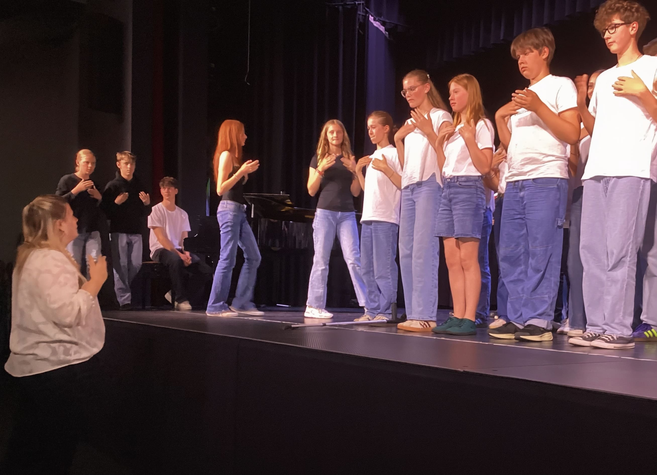 Die Schülerinnen und Schüler der 7b und 7c betreten rhythmisch klatschend aus dem Zuschauerraum heraus die Bühne. Im Vordergrund unterhalb der Bühne Frau Hoepner, welche den Takt vorgibt.